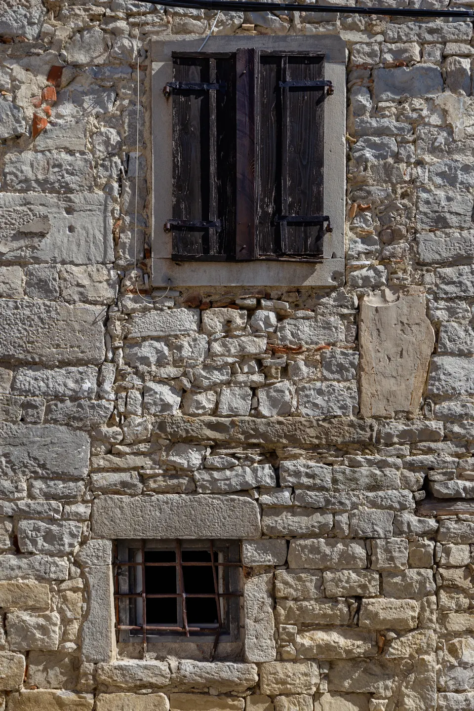 An old stone wall with shuttered windows in Buzet: lime mortar joints and stone that has been allowed to weather.