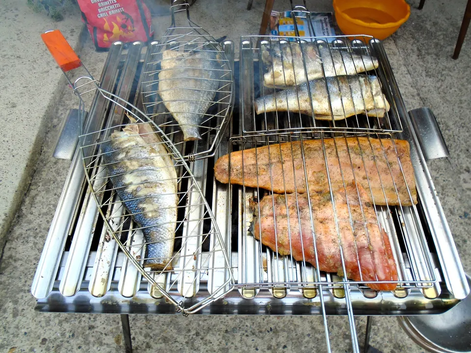 Whole fish and fillets cooking side by side on an outdoor grill.