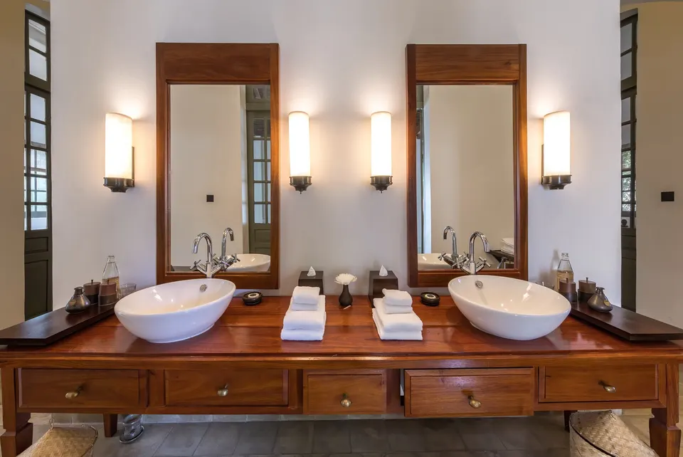 A double vanity with drawers and a wall light on each side of every mirror: even light on the face, not from the ceiling.