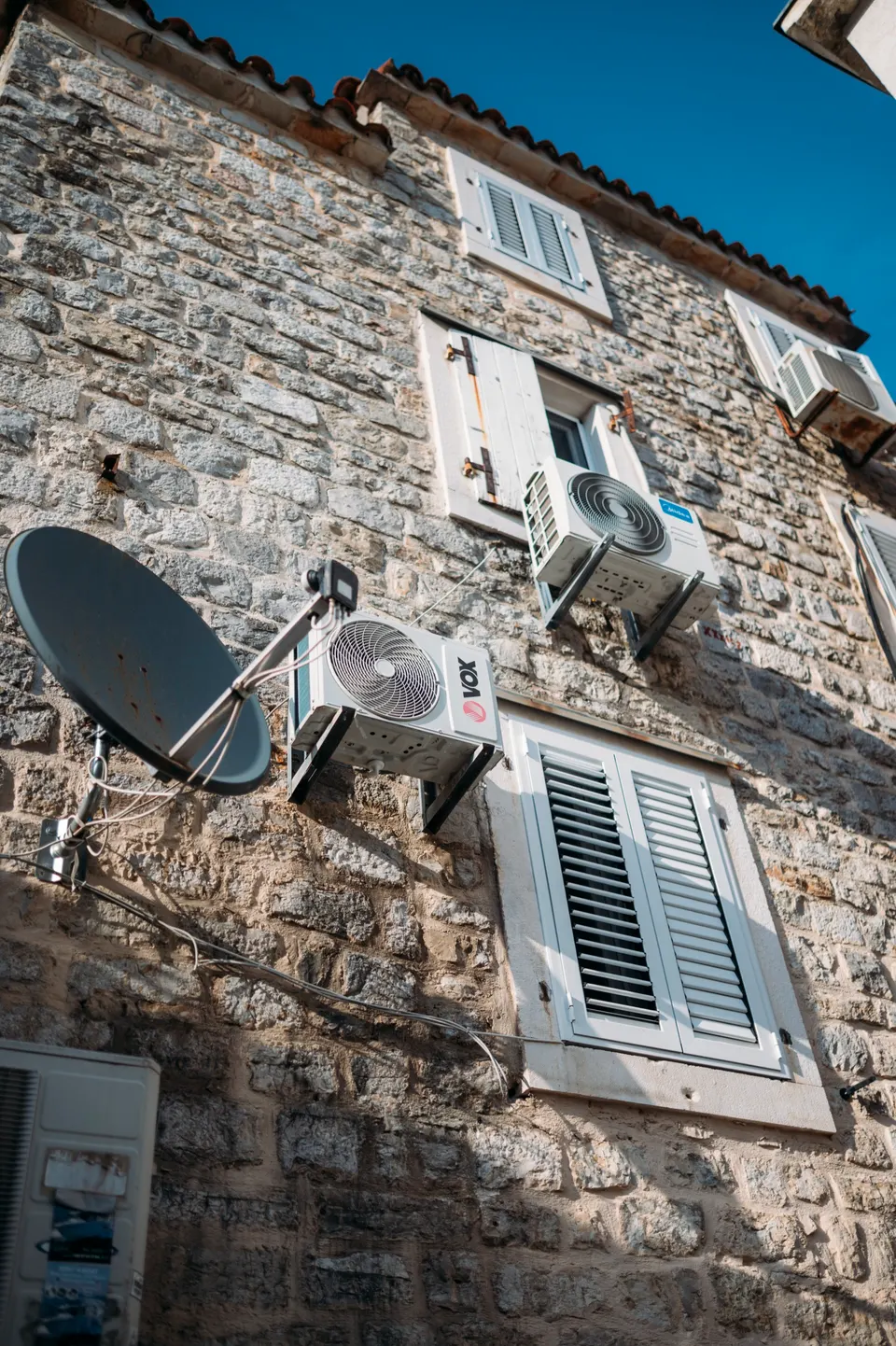 Outdoor units, cables and a satellite dish added to a stone façade: what happens when cooling is not planned with the house.