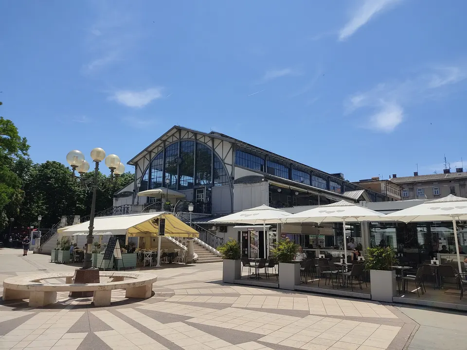 Pula's iron-and-glass market hall, with café terraces on the square in front.