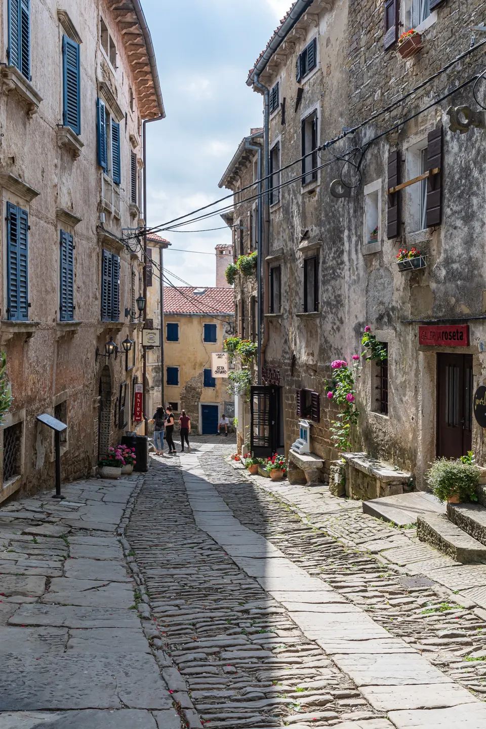 A cobbled street in Grožnjan, lined with restored stone houses and blue shutters.