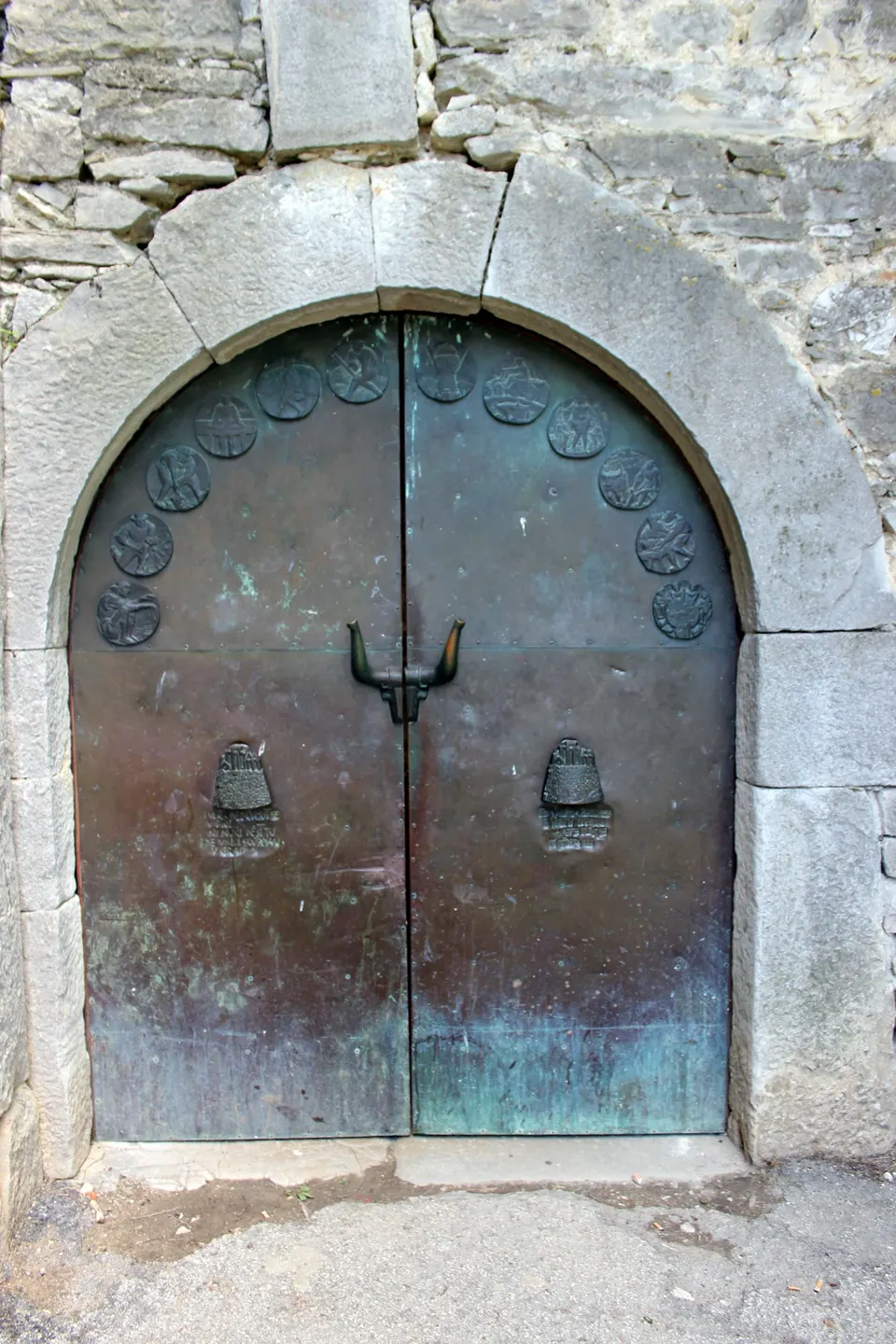 The arched town gate of Hum, with copper doors decorated with round medallions and horn-shaped handles.