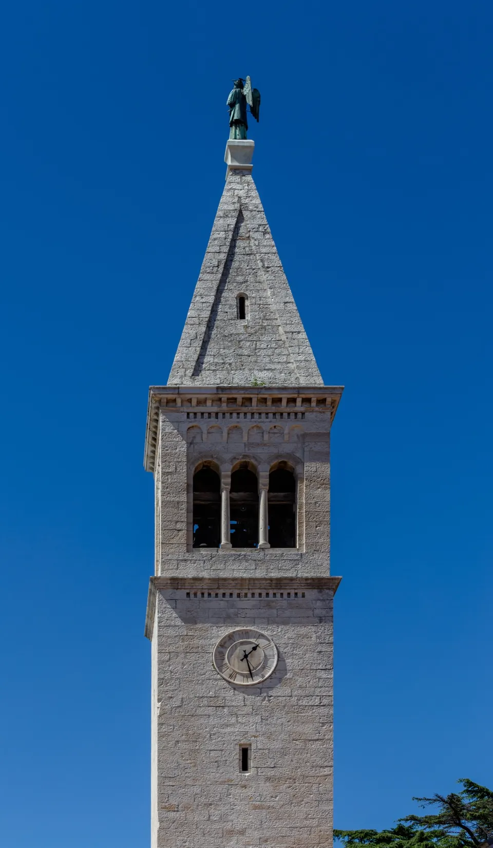 The stone bell tower of the Church of St Pelagius against a deep blue sky, with a statue at its top.