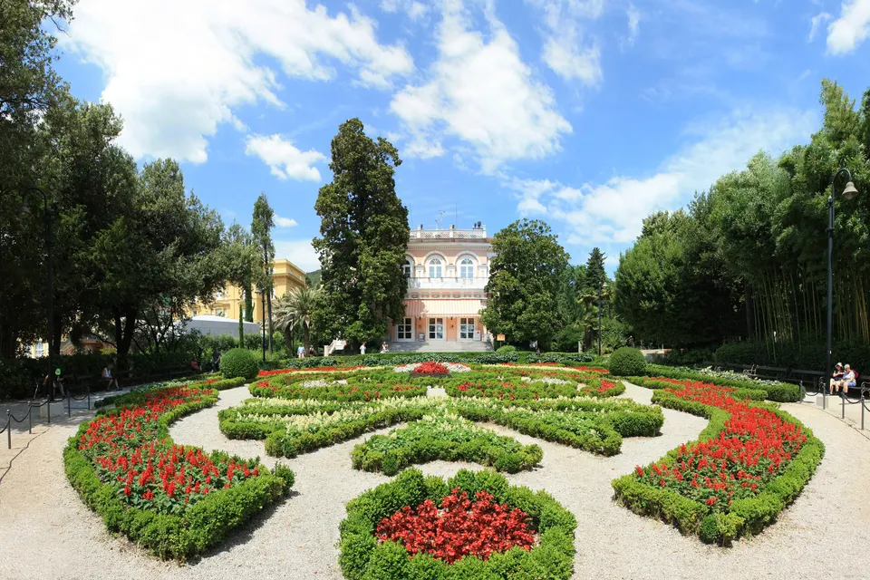 Villa Angiolina seen across the formal flower beds of its park.