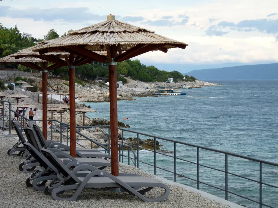 Umbrellas above the water at Girandella beach in Rabac, with the Kvarner beyond.