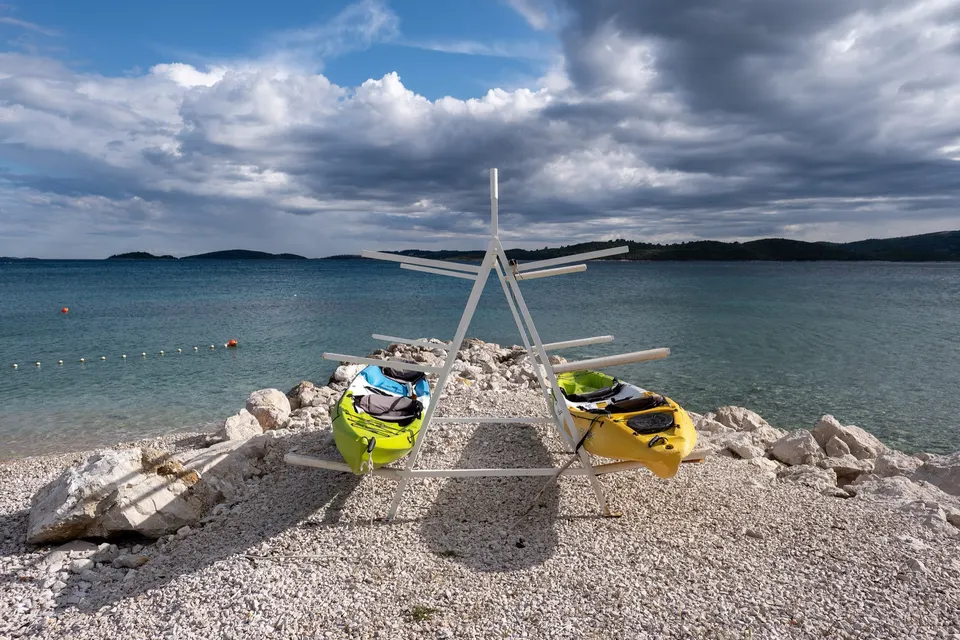 Zwei Seekajaks auf einem Gestell an einem Kiesstrand der kroatischen Küste.