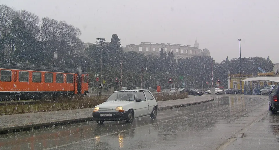 Seltener Schneefall in Pula; hinter den Bäumen zeichnet sich schwach das römische Amphitheater ab.