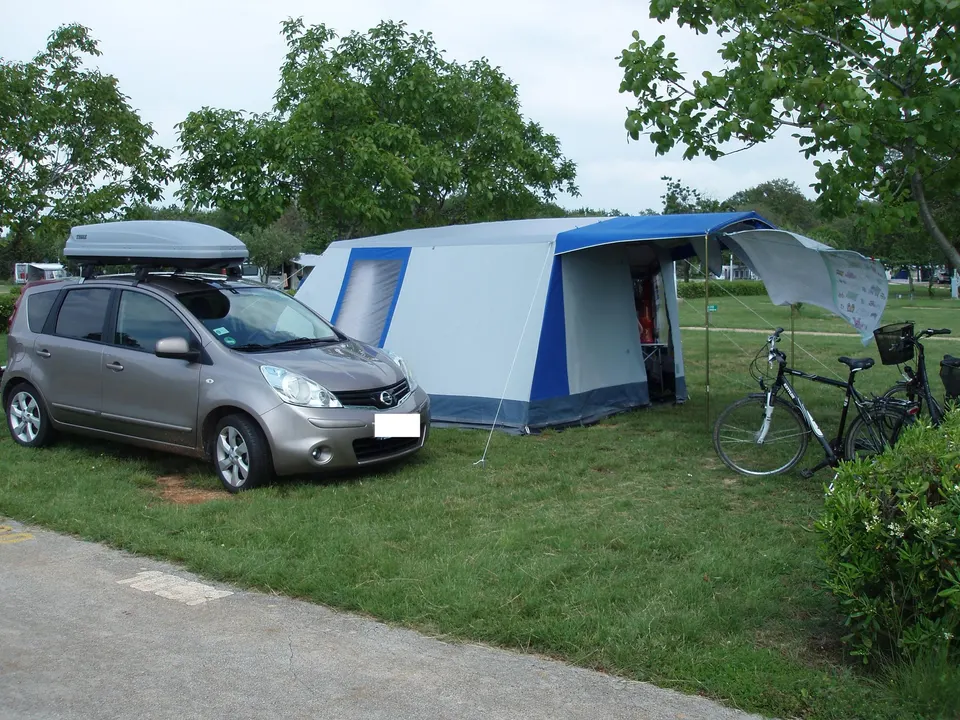 Ein Familienzelt mit Vorzelt, ein geparktes Auto mit Dachbox und zwei Fahrräder auf einem Wiesenstellplatz eines Campingplatzes bei Lovrečica.
