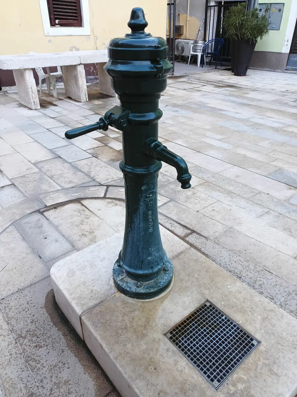 Ein grüner gusseiserner Trinkwasserbrunnen auf einem Steinsockel auf einem gepflasterten Platz in Novigrad.