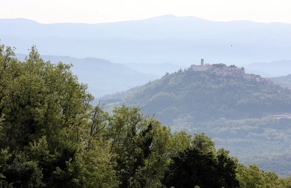 The hill town of Motovun on its hilltop, seen across wooded hills from Vižinada, with the haze of the interior behind.