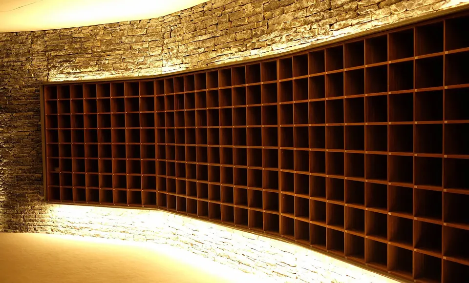 Una lunga parete di vani aperti in legno per le scarpe, inserita in un muro curvo in pietra e illuminata dolcemente dal basso.