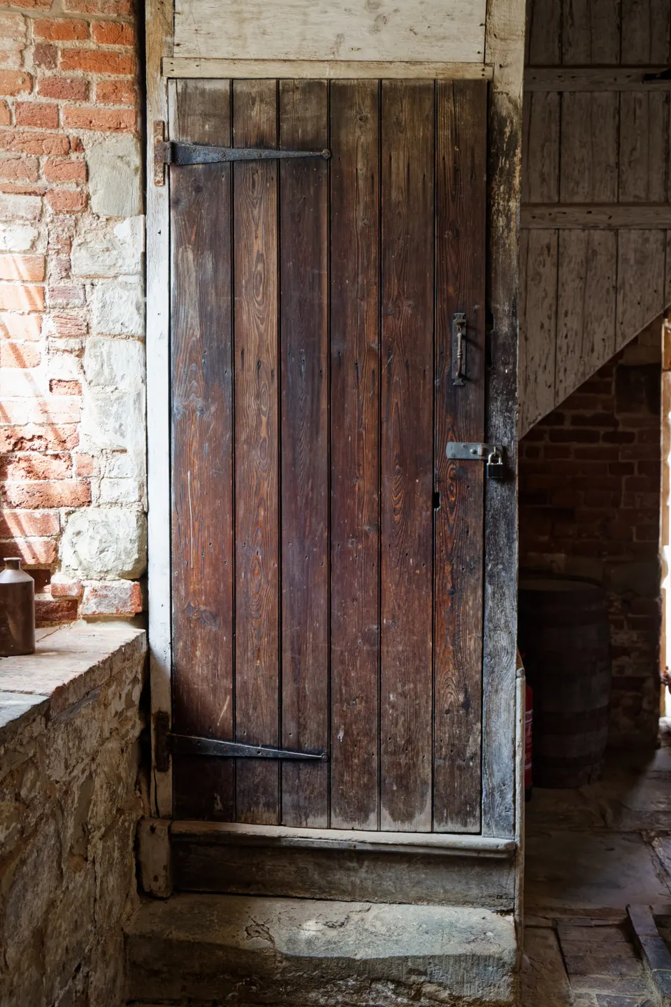 An old ledged plank door with iron strap hinges, set in a wall of brick and stone: the honest, simple door that many old houses started with.