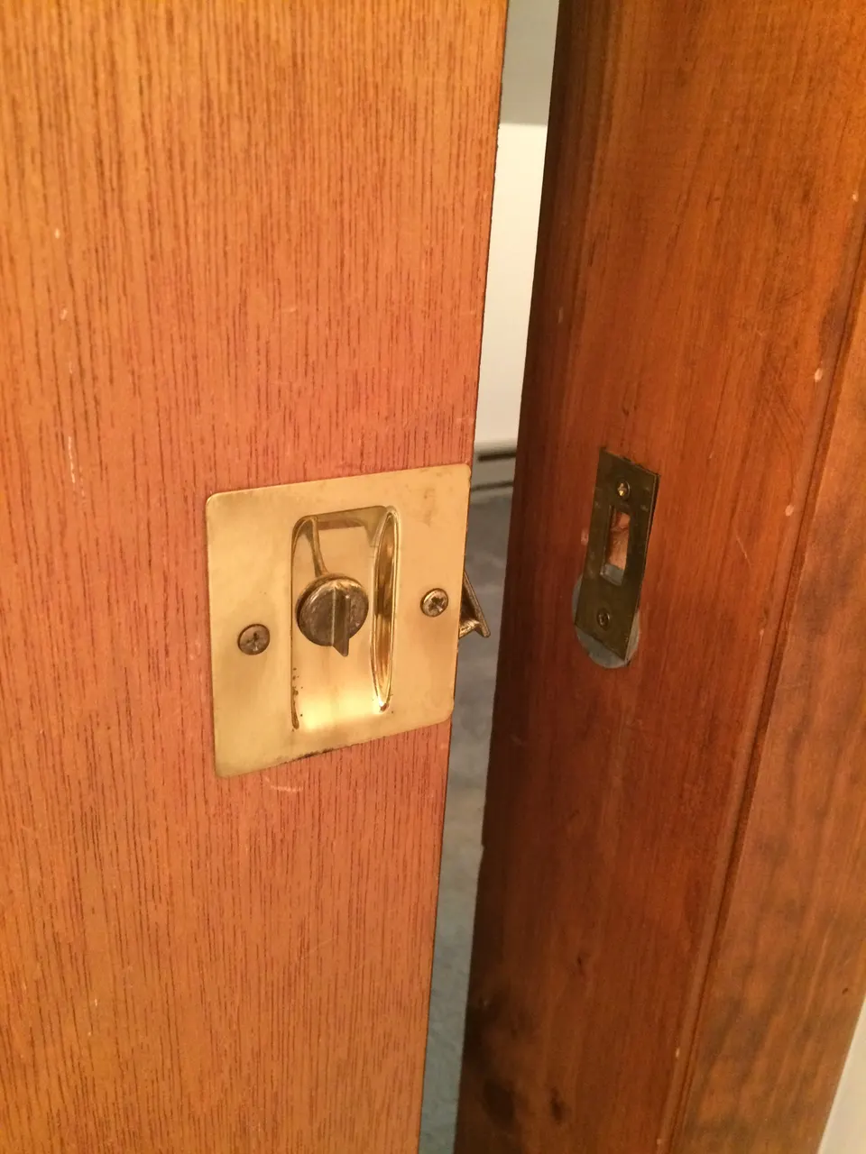 The edge of a pocket door with a recessed brass pull and privacy latch, and the strike plate on the frame opposite: hardware that sits flush so the door can slide into the wall.