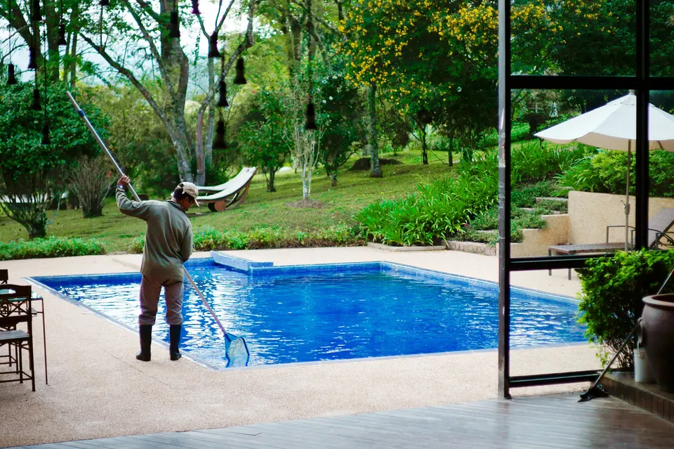 Skimming a garden pool with a long net: routine pool care is one of the tasks someone local has to own throughout the season.
