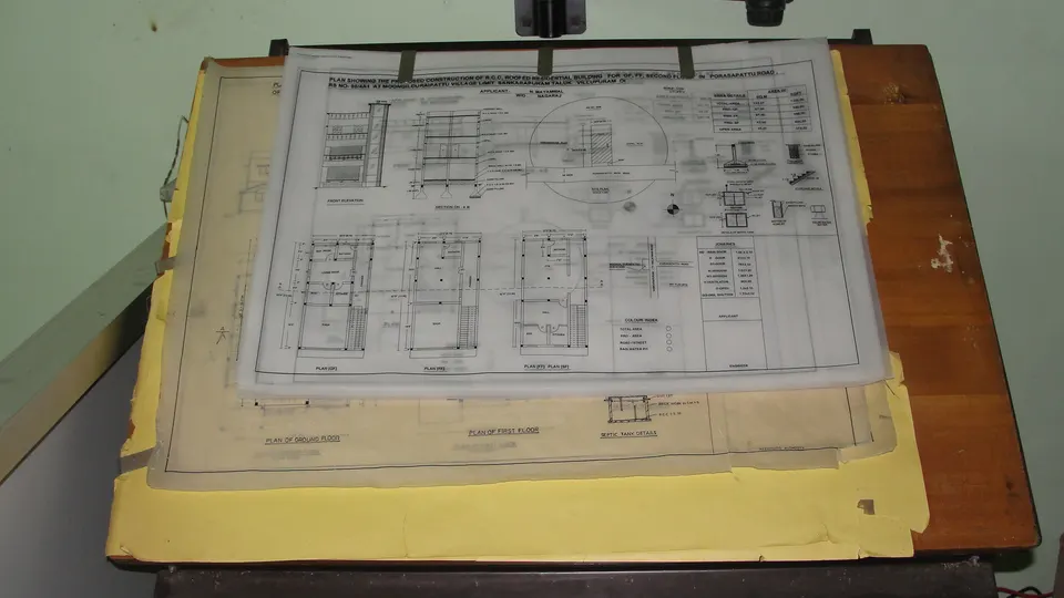 Building drawings on tracing paper, clipped to a drafting table: plans, sections and elevations of a house. A bill of quantities is measured from drawings like these.