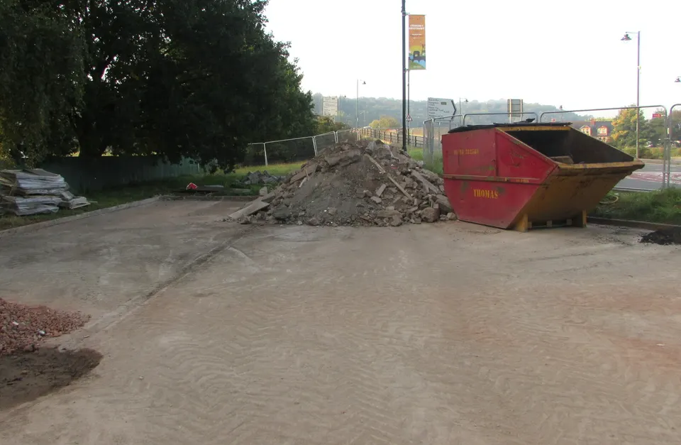 Ein Haufen aus Betonbruch und Ziegeln neben einer Mulde auf einem geräumten Grundstück. Aufladen, Transport und Entsorgung von Bauschutt gehören zu den Positionen, die im Angebot am häufigsten fehlen.