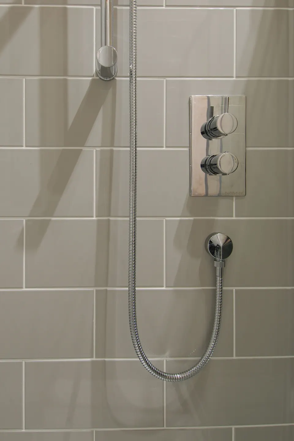 A finished shower wall with a thermostatic valve and hand shower on a rail. At handover, run it hot and cold and check the joints around each fitting.