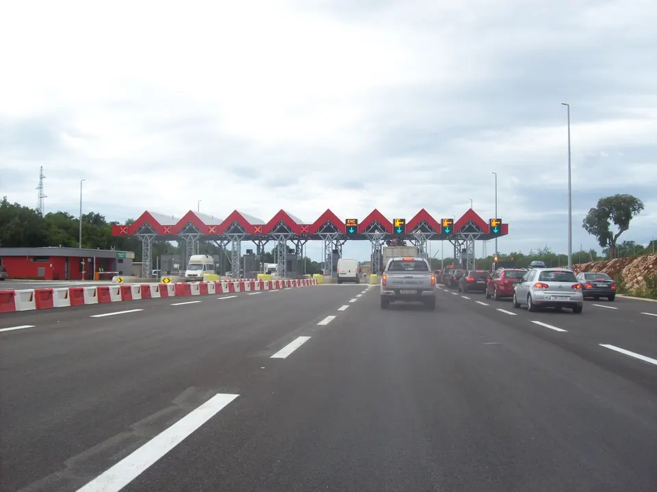 Cars approaching a toll plaza with red canopies on the A9 motorway near Pula.