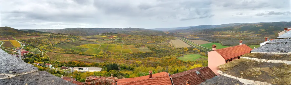 Autumn colours in the valley below Motovun, seen over the town's red-tiled roofs under a grey sky.