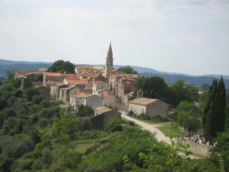 Draguć on its ridge: stone houses with tiled roofs, the pointed bell tower of the parish church and wooded hills fading into the distance.