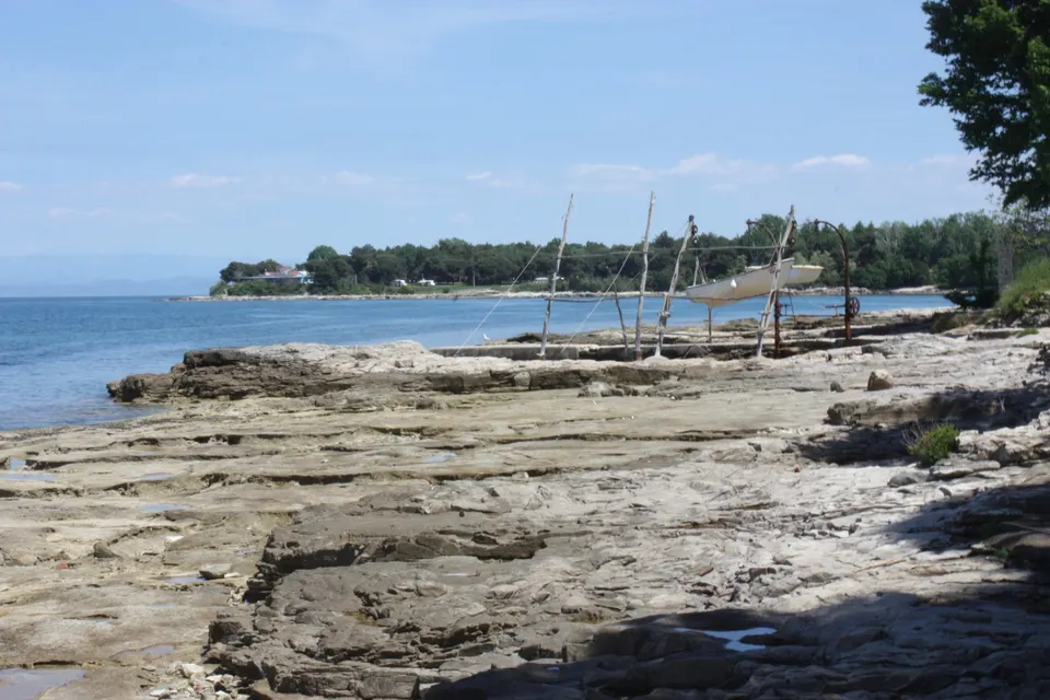 Flat limestone shore at Savudrija, with traditional wooden boat hoists and a small boat lifted above the rocks.
