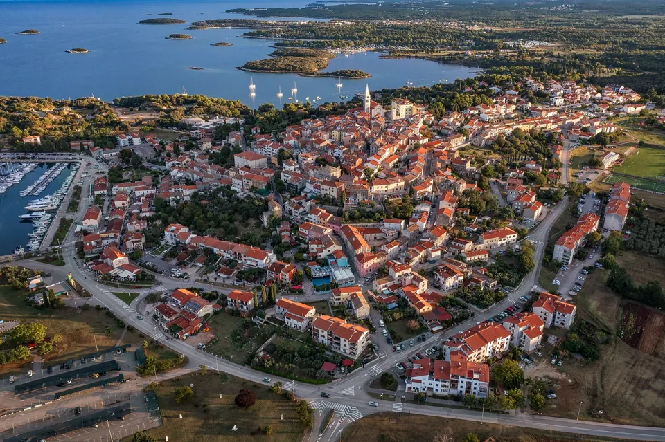Vrsar from the air: red roofs and the bell tower on the hill, the marina on the left and a line of wooded islets in the sea beyond.