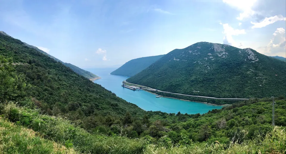 Plomin Bay seen from the hillside: a long, narrow turquoise inlet between steep green slopes.