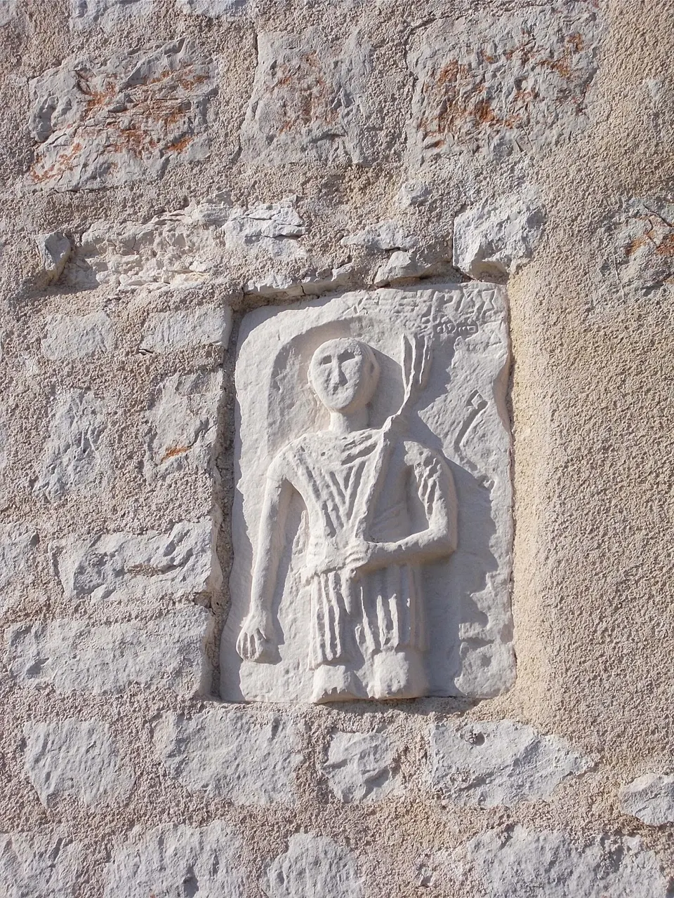 The carved relief of a standing figure set into the stone wall of the church of St George the Elder in Plomin.