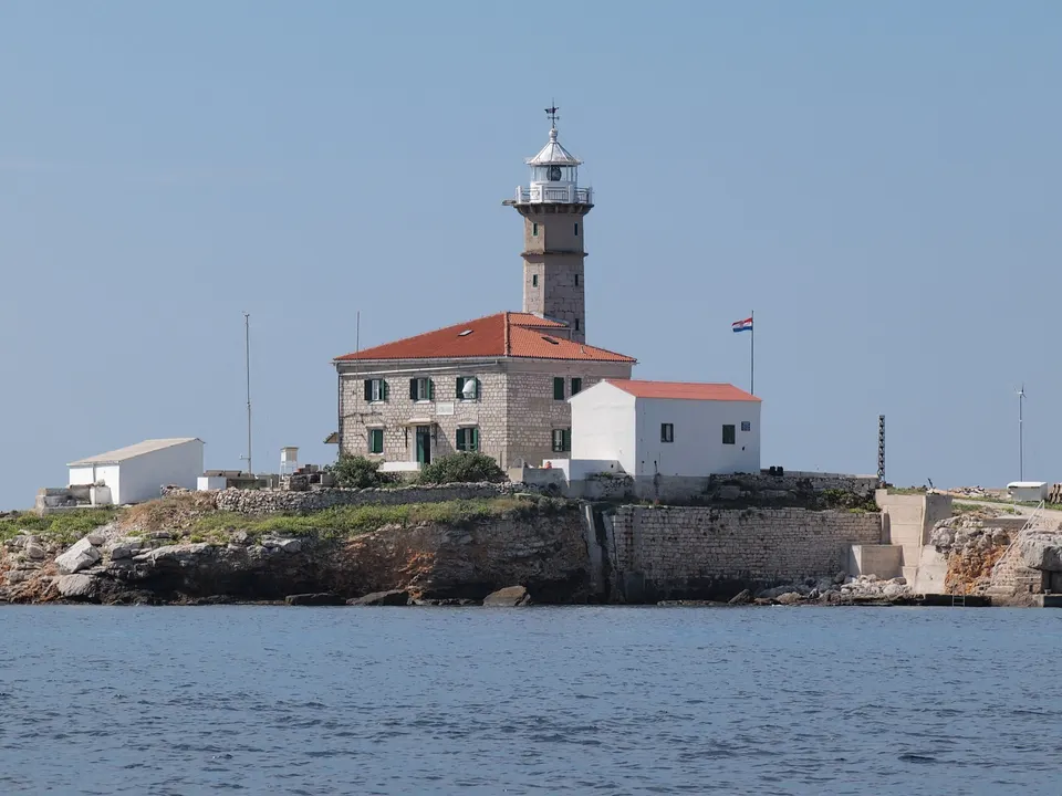 Sveti Ivan na pučini lighthouse off Rovinj: a stone tower on a keeper's house with red roofs, on a low rocky islet.