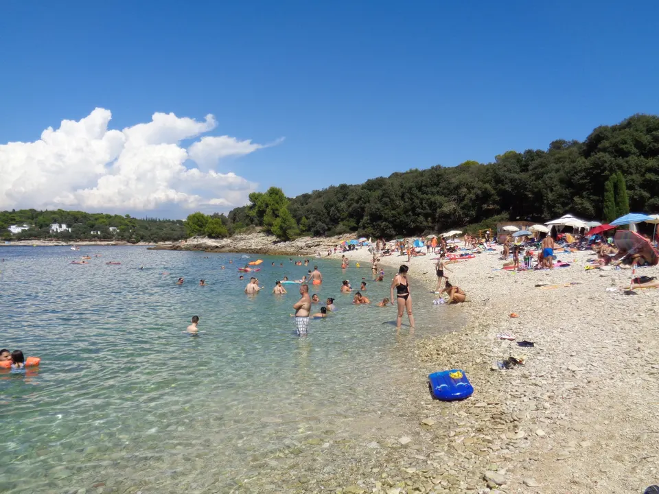 Ambrela beach on Punta Verudela: a shallow pebble shore, clear water and pine woods along the bay.