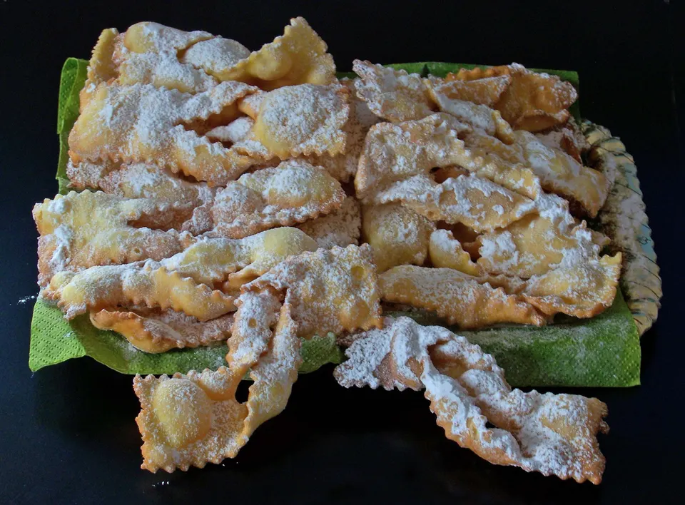 A tray of crisp fried pastry ribbons with fluted edges, dusted with icing sugar: the carnival sweet known in Istria as kroštule.