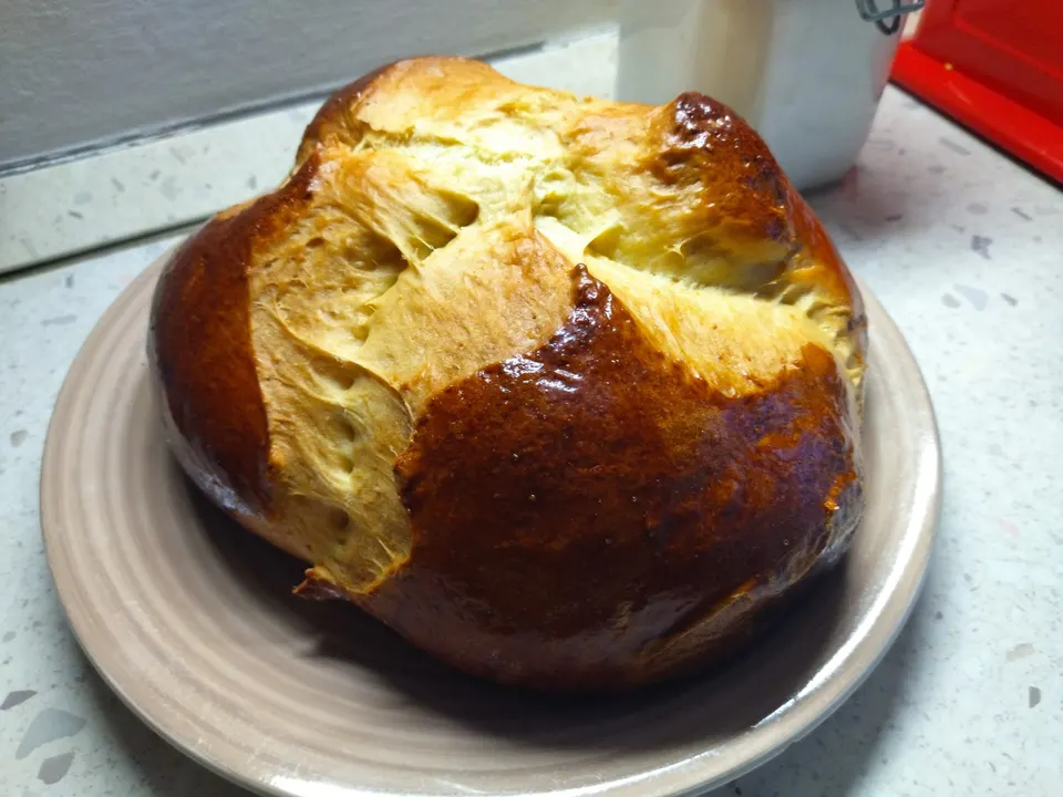 A round sweet Easter bread with a dark glossy crust, its top cut open into flaps during baking.