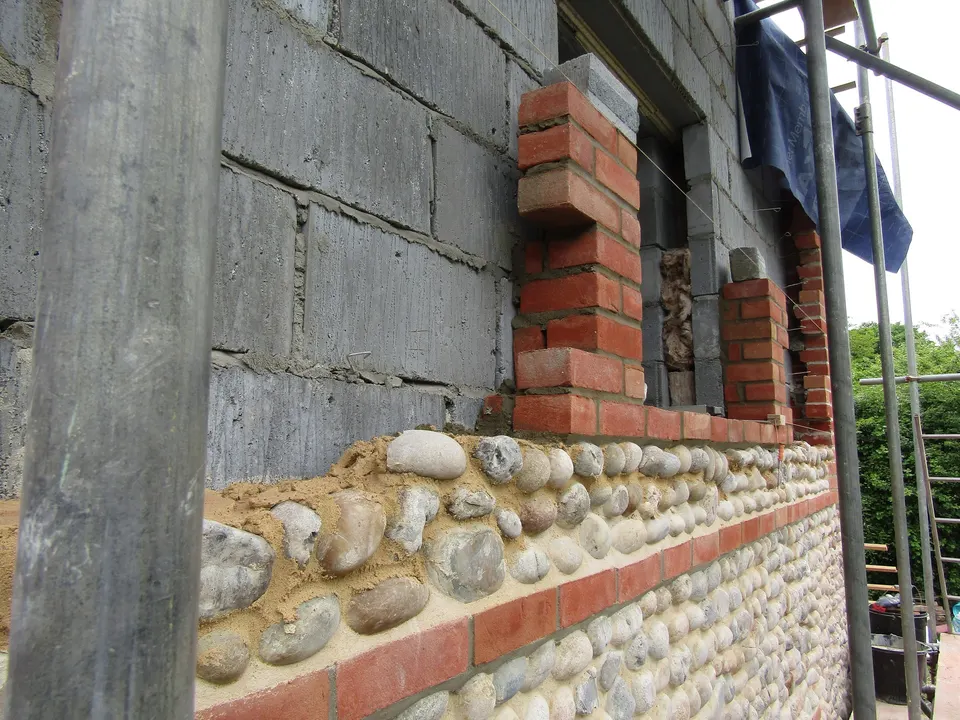 Brick window surrounds rising above a cobble wall on a building site. Detail work like this shows the quality of a team.