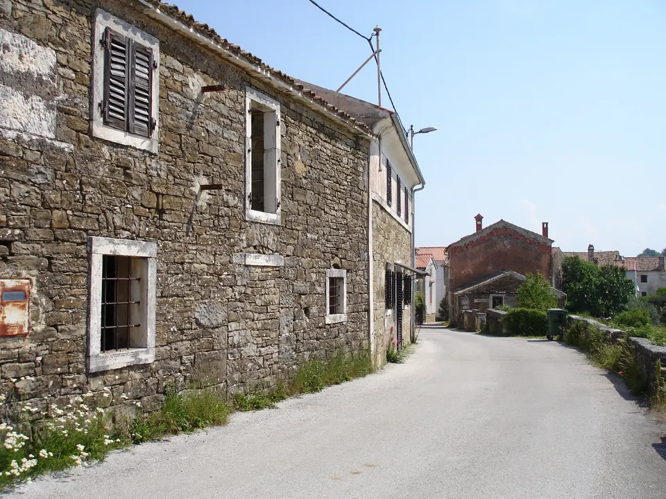 Stone houses with timber shutters and stone window frames along a village lane in Momjan.