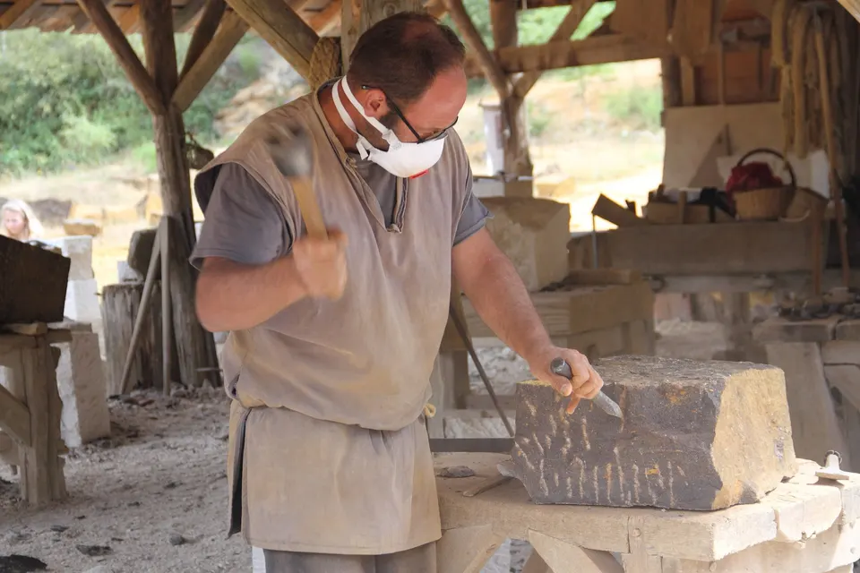 A stonemason shaping a block with hammer and chisel. Skilled hand work is one of the real costs of a stone renovation.