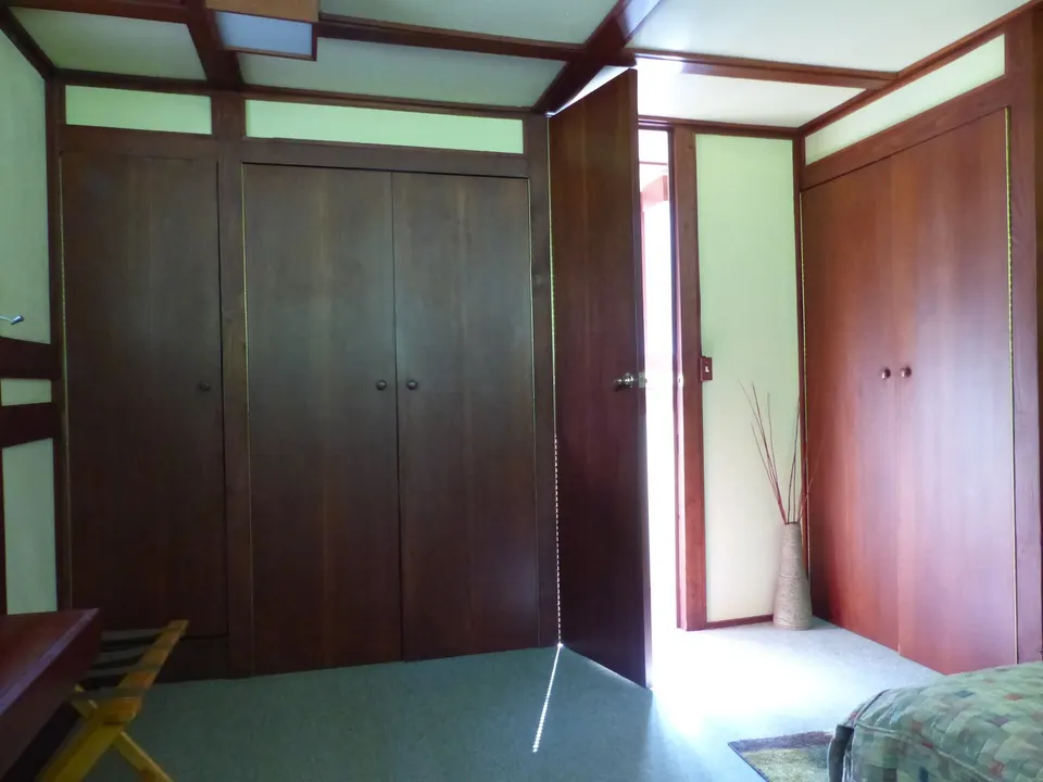A wall of built-in wardrobes with plain wooden doors and small knobs, set into a timber-framed bedroom.