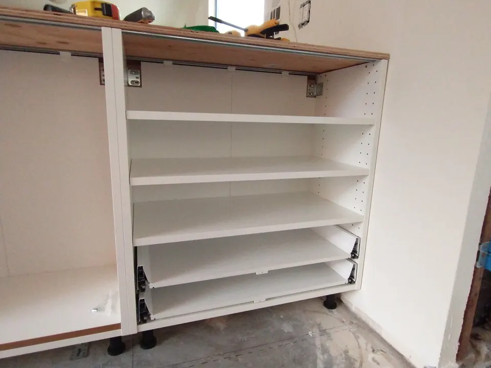 Base cabinet carcasses during installation, before the doors are hung: shelves, drawer runners and the fixings that hold the worktop.