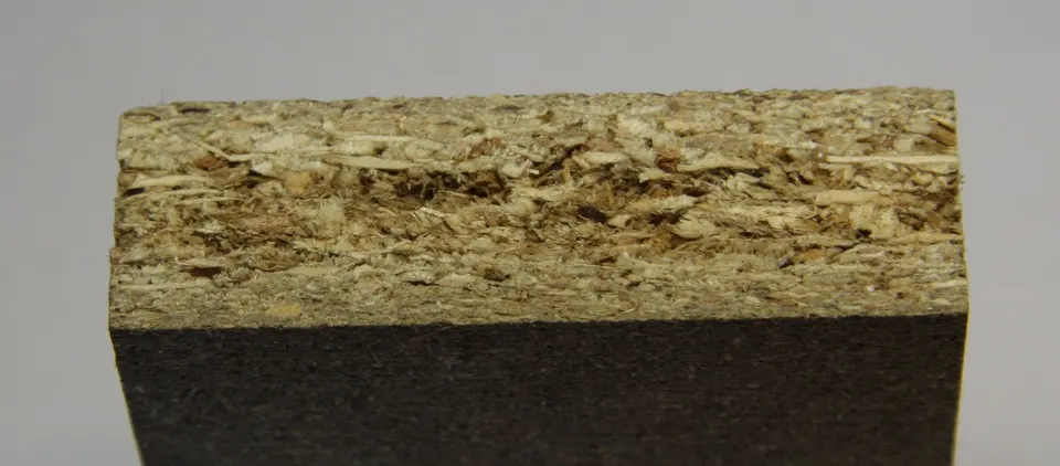 The cut edge of a particleboard panel: compressed wood chips and resin under a thin surface layer.