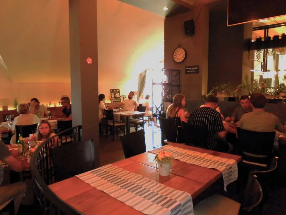 A busy dining room with wooden tables, dark chairs and a mix of table sizes, photographed during service.