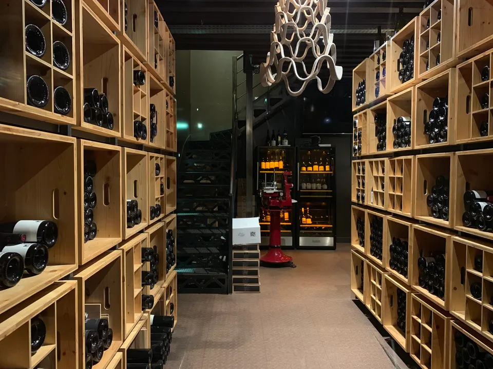 Floor-to-ceiling wooden cube shelving holds bottles on both sides of a narrow wine bar passage.