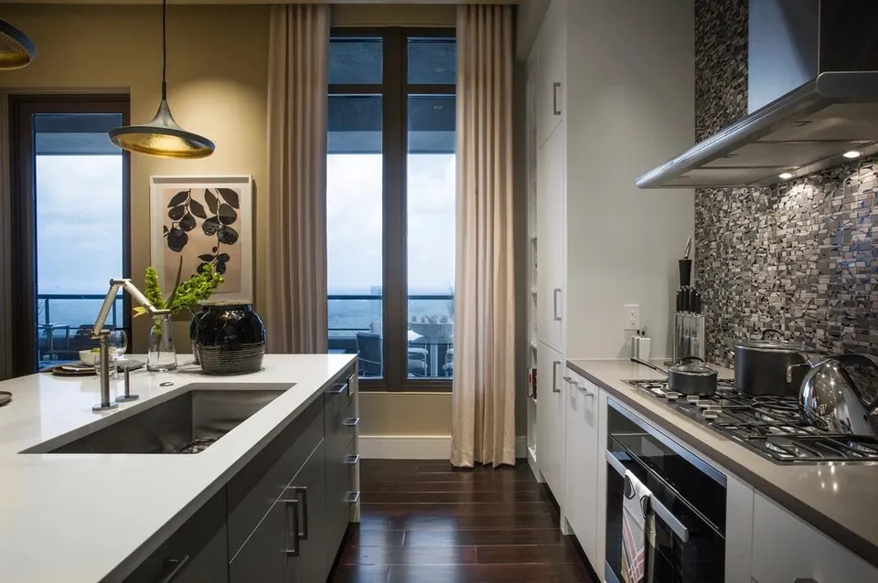 A long stone worktop with sink and hob, lit by tall windows and a pendant lamp.