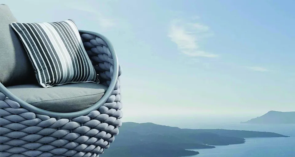 A striped cushion on a woven outdoor armchair, with the sea and islands behind.